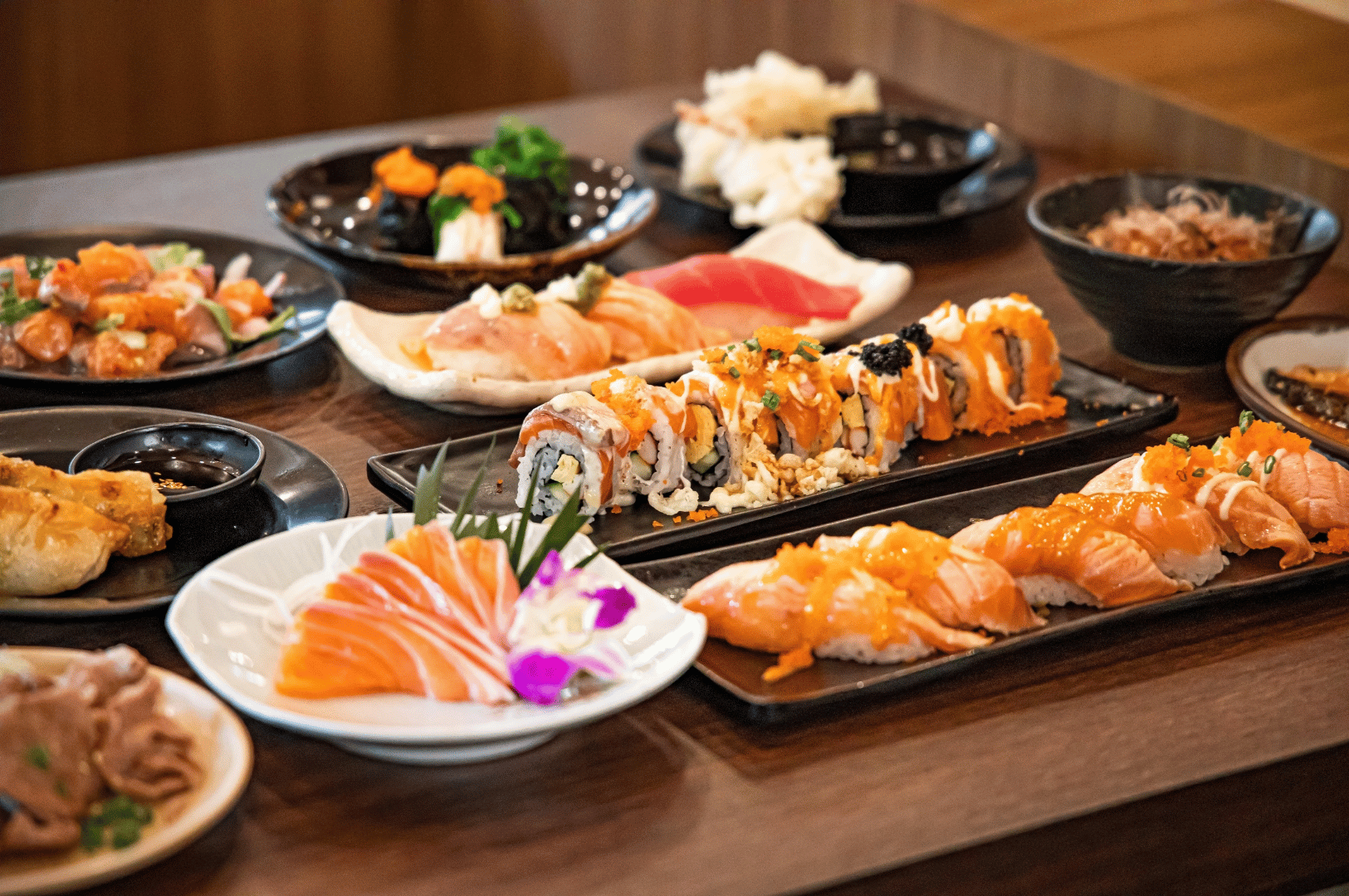 An abundant spread of Japanese sushi—salmon sashimi, nigiri, sushi rolls with vibrant garnishes, seaweed salad, and pickled vegetables—arranged on a wooden table with edible flowers and green leaves, showcasing the visual elegance and flavor diversity of Japanese cuisine as a canvas for Singapore’s fusion reinterpretation.