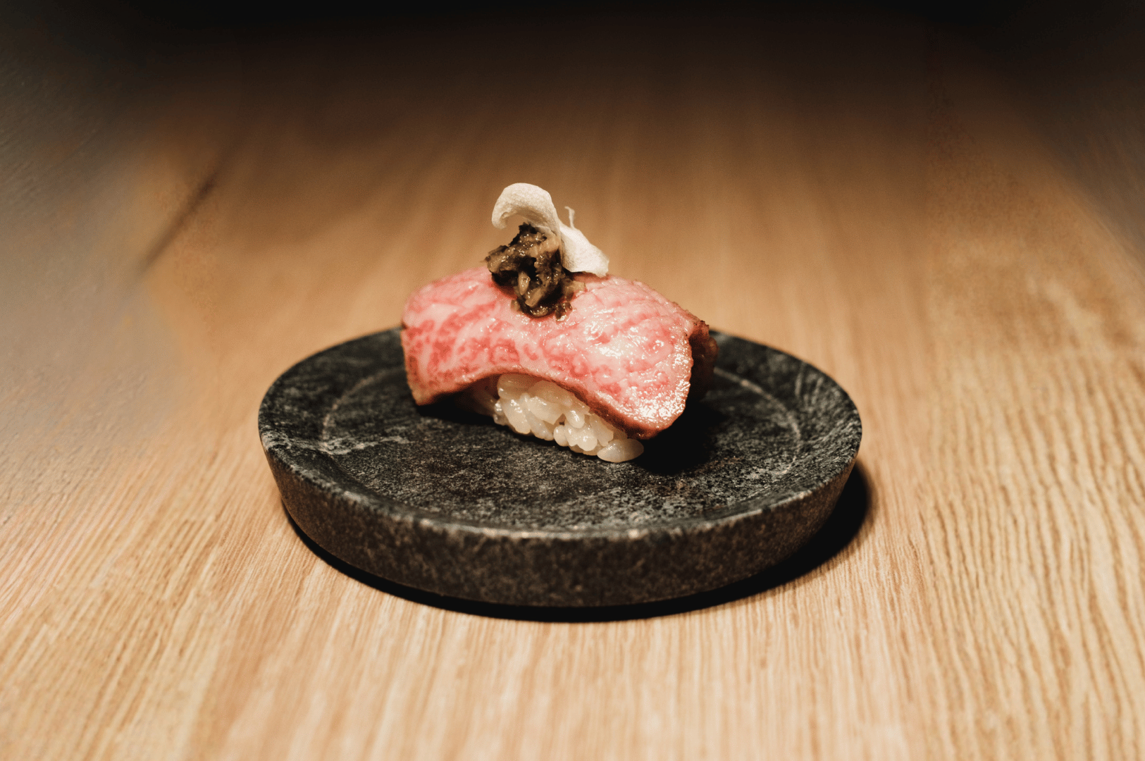 Wagyu beef sushi garnished with garlic and truffle on a stone plate—showcasing luxurious omakase ingredients and refined presentation techniques.