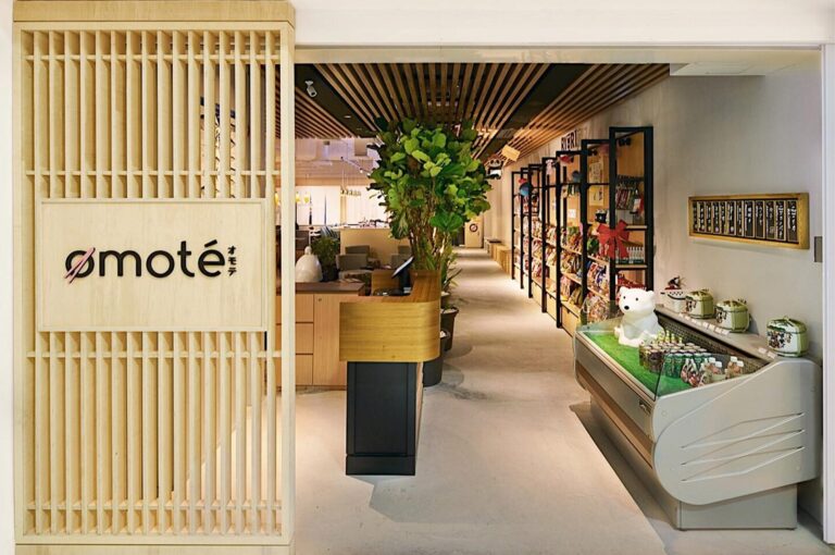 Entrance and retail area of Omote Japanese restaurant, featuring a wooden slatted wall, a tree centerpiece, and shelves stocked with merchandise.